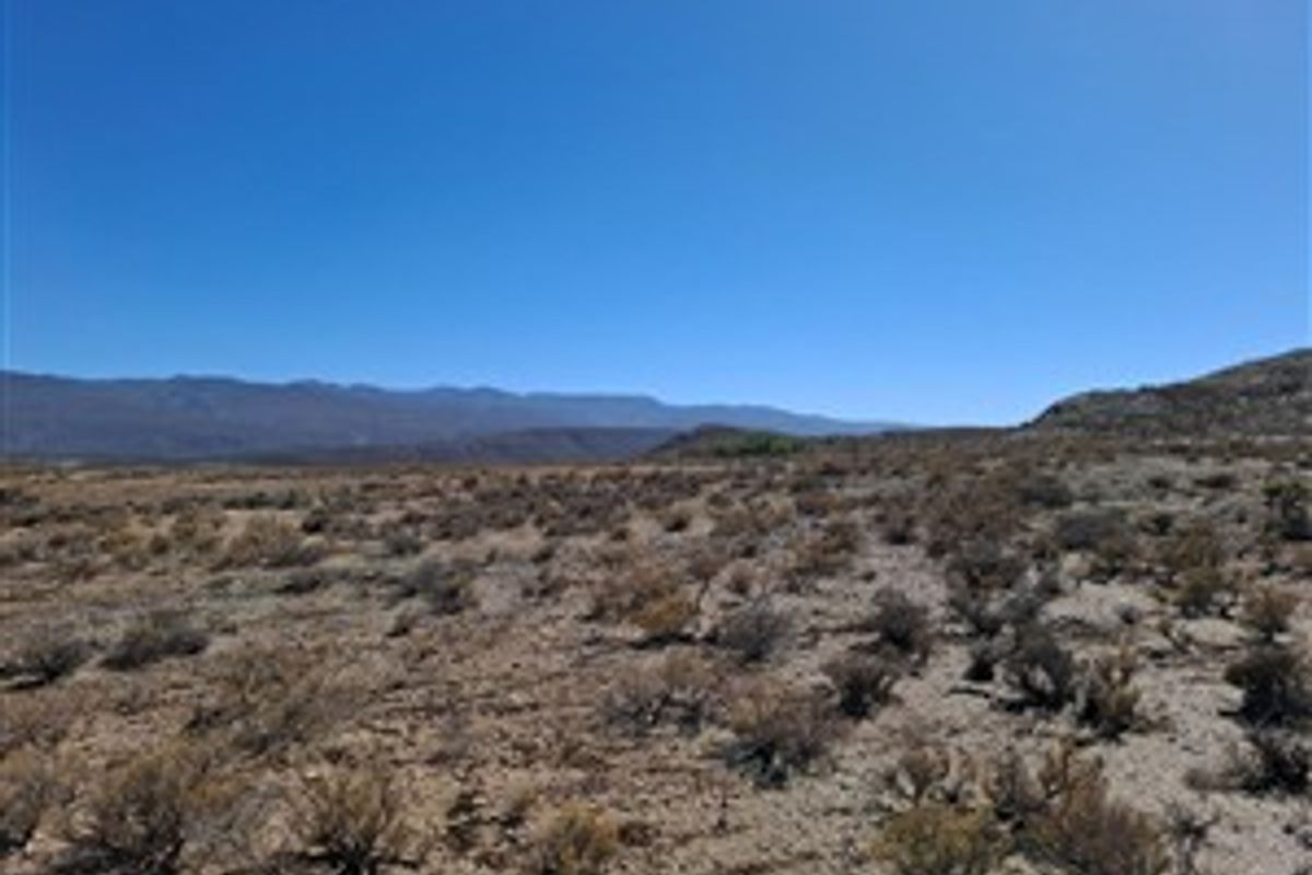 A wide-angle view of the expansive, arid landscape and mountain range surrounding the farm property.