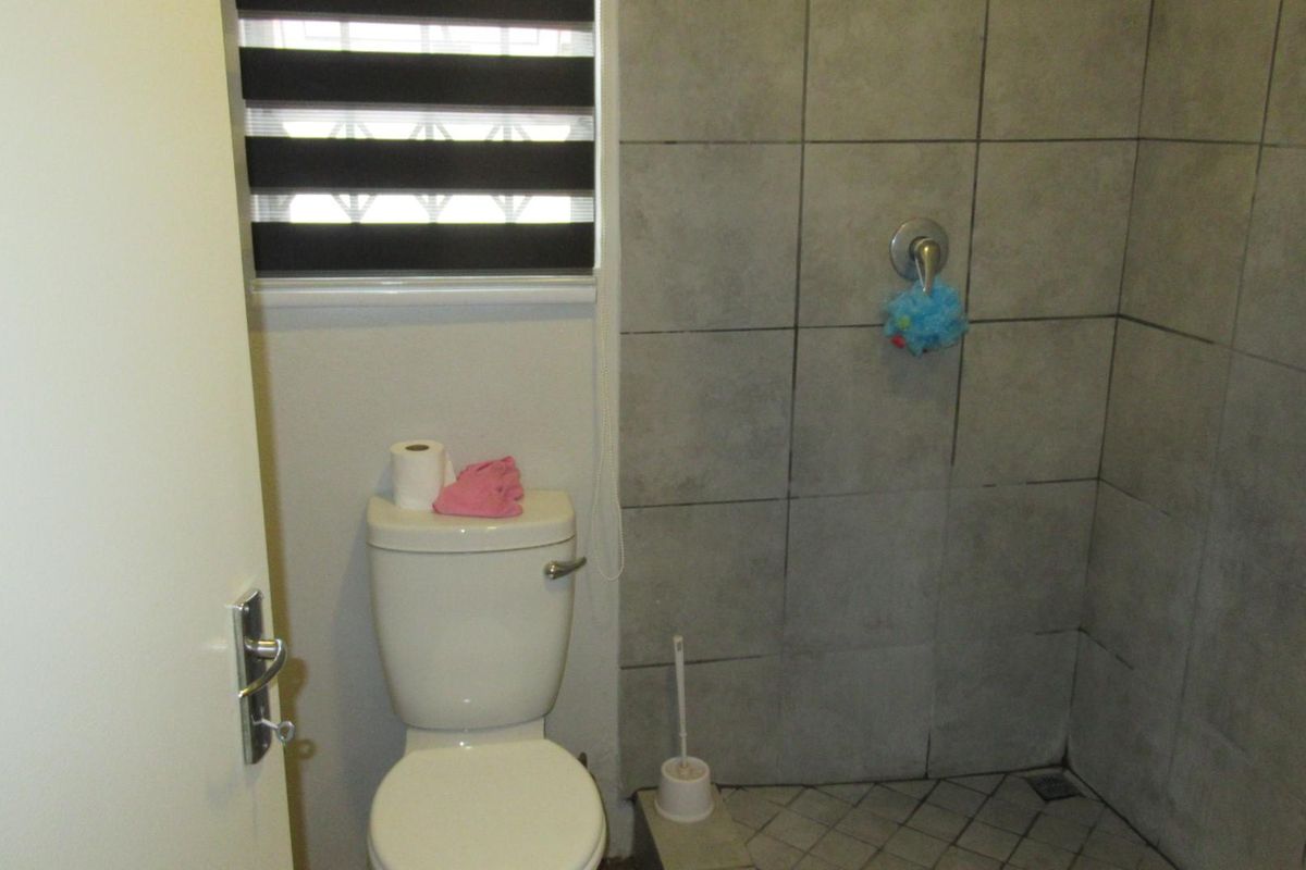 A functional bathroom featuring a tiled shower enclosure, a standard toilet, and a window with fitted blinds.
