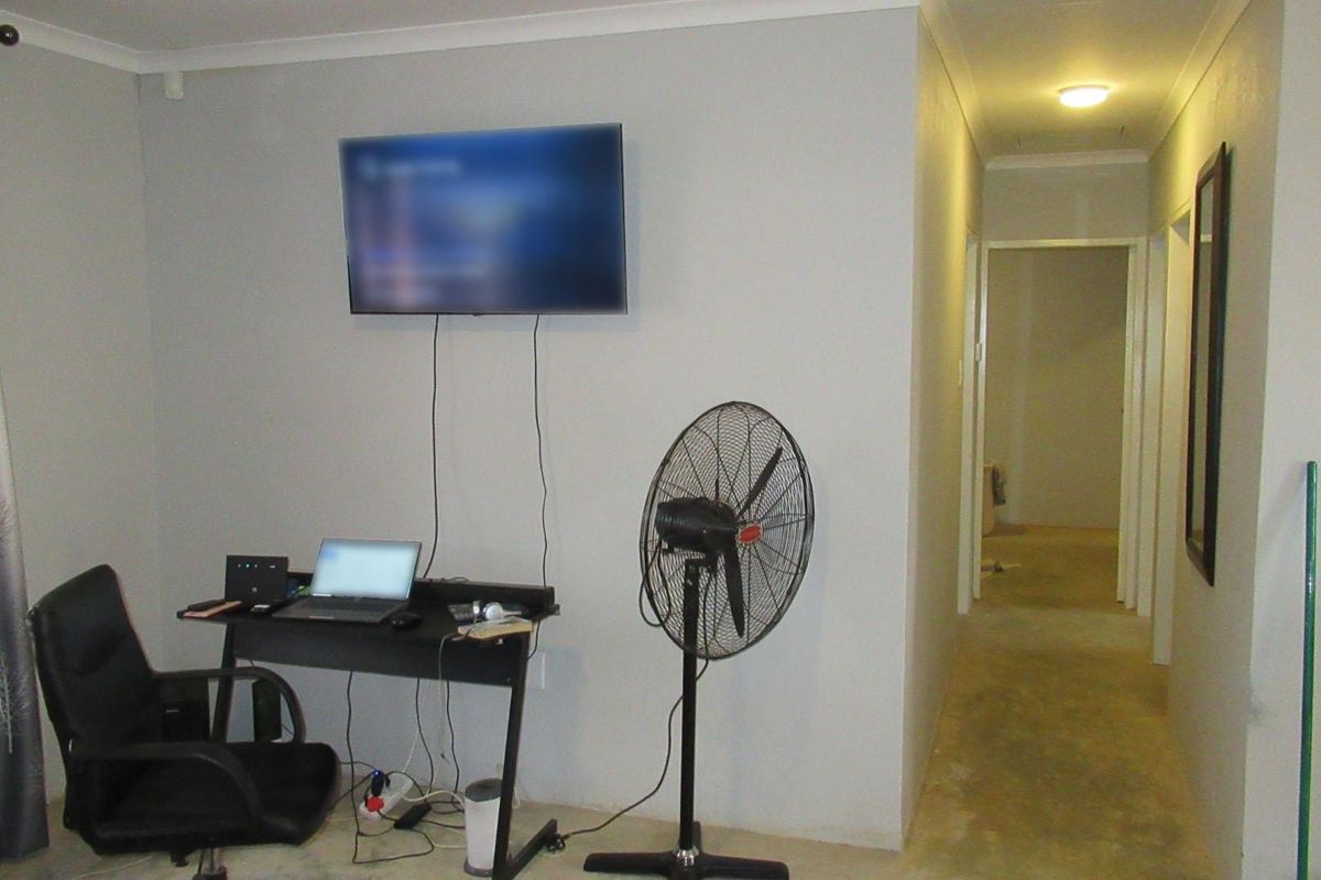 A living area featuring a wall-mounted television and an adjacent hallway leading to other rooms, with neutral wall finishes.
