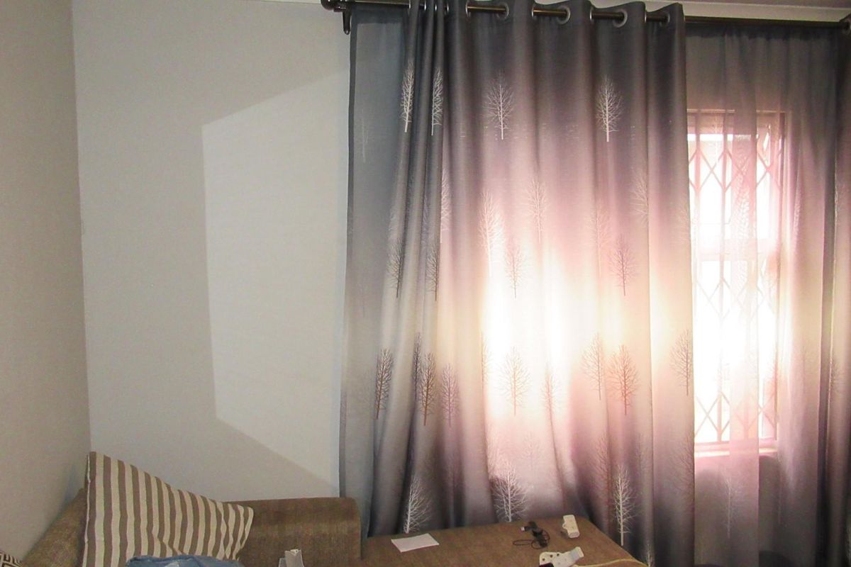 A view of a bedroom interior featuring a window with security bars and curtain fixtures.