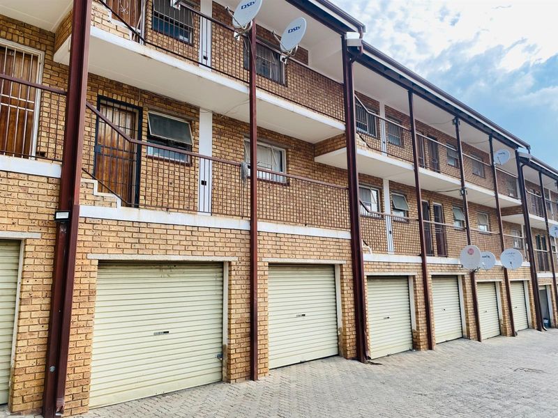 Exterior view of a multi-story apartment complex featuring face brick facade, multiple roller garage doors, and private balconies with metal railings.