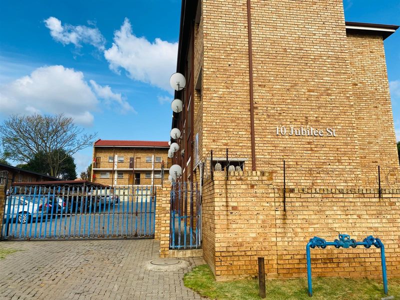 Exterior view of a face brick apartment complex featuring a gated entrance, paved driveway, and covered parking area.