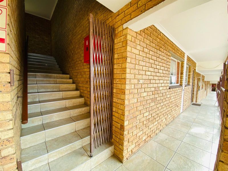 Exterior apartment hallway featuring a tiled staircase, exposed brick walls, and a security gate providing access to the building levels.