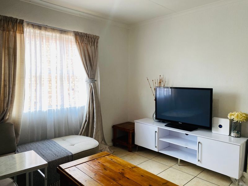 A living room featuring neutral tiled flooring and a large window with curtain treatments, providing a functional and well-lit space.