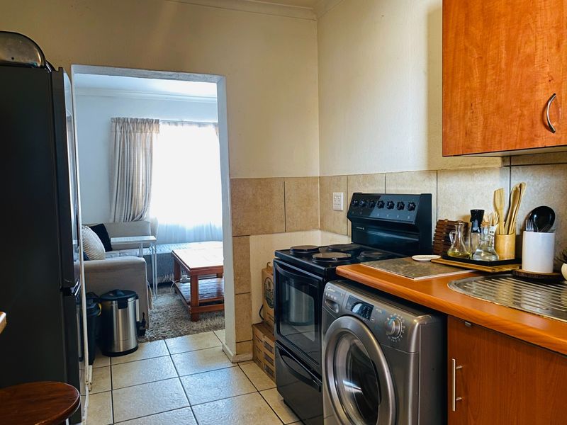 A functional kitchen featuring wood-finish cabinetry, tiled backsplash, and a freestanding stove, with an open transition into the adjacent living area.