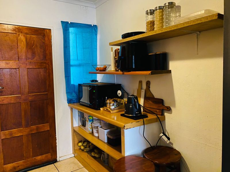 A compact kitchen area featuring open wooden shelving, a wooden door, and tiled flooring, providing functional storage space.
