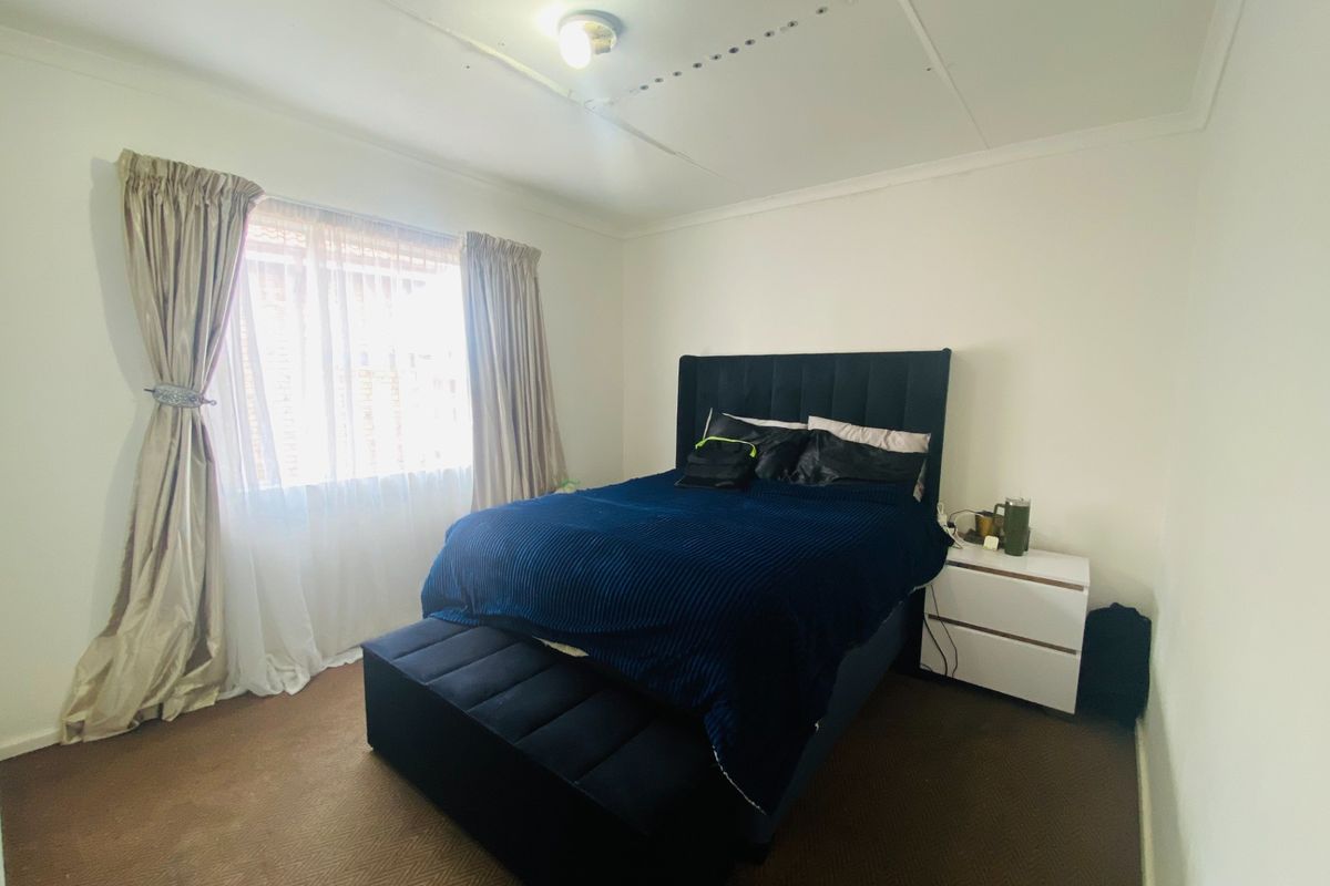 A bedroom featuring carpeted flooring and a window with curtains. The ceiling shows visible panel seams, suggesting a need for cosmetic updates.
