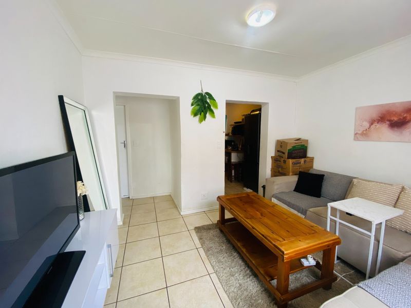 A living room featuring tiled flooring and neutral walls, providing a functional space with direct access to adjacent areas.