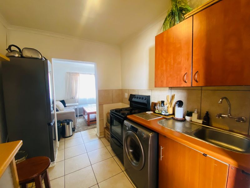 Compact kitchen featuring wooden cabinetry, tiled backsplash, stainless steel sink, and built-in appliance space, with direct access to the adjacent living area.