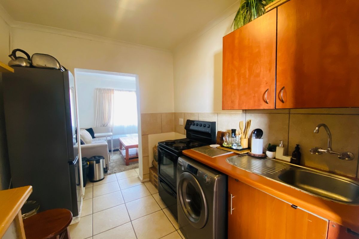 Compact kitchen featuring wooden cabinetry, tiled backsplash, stainless steel sink, and built-in appliance space, with direct access to the adjacent living area.