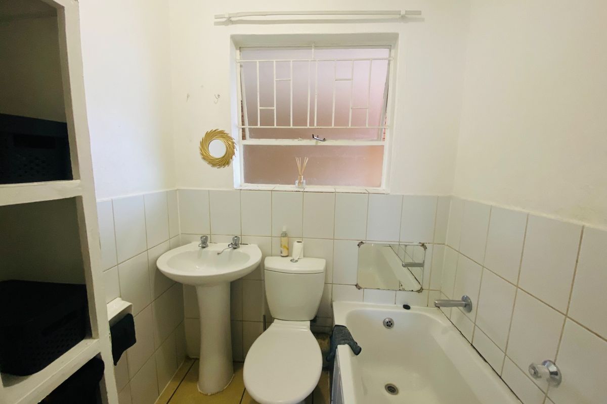A compact bathroom featuring a pedestal basin, toilet, and bathtub with tiled finishes and built-in shelving.