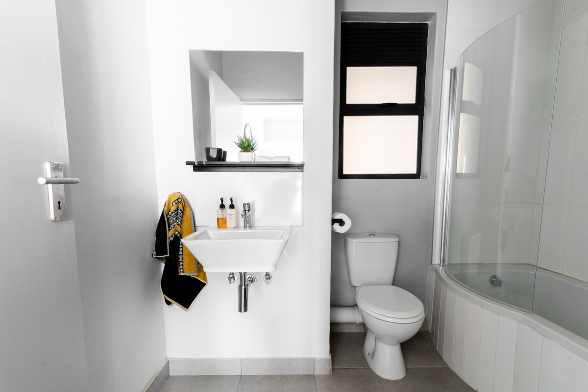 Compact bathroom featuring a wall-mounted basin, a standard toilet, and a shower-over-bath combination with a glass screen.