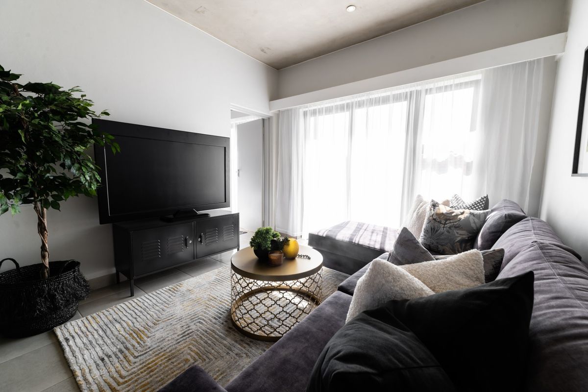 Modern living room featuring large sliding glass doors, neutral tiled flooring, and a high ceiling, providing a bright and contemporary living space.
