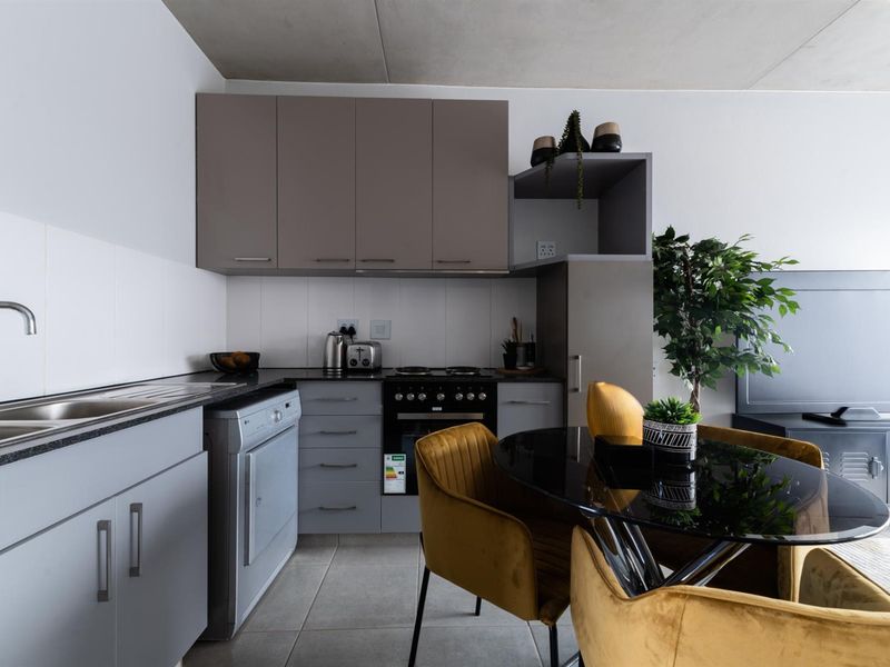 Modern open-plan kitchen featuring sleek grey cabinetry, integrated appliances, tiled backsplash, and durable tiled flooring, seamlessly flowing into the adjacent living area.