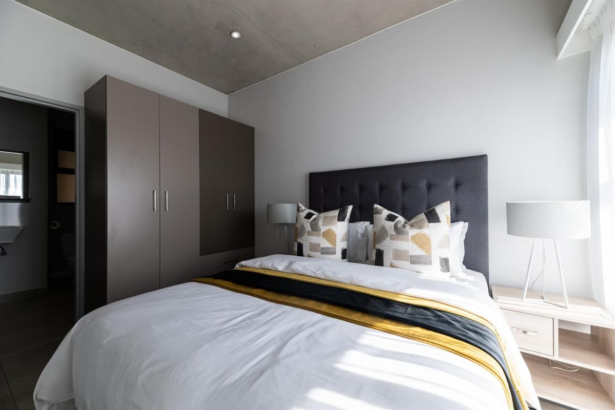 Modern bedroom featuring an exposed concrete ceiling, recessed lighting, and a sleek built-in wardrobe, offering a contemporary and well-maintained living space.