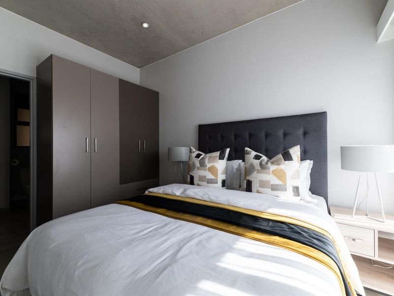 Modern bedroom featuring an exposed concrete ceiling, recessed lighting, and a sleek built-in wardrobe, offering a contemporary and well-maintained living space.