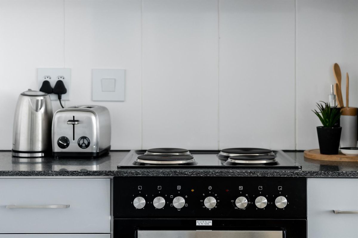 A clean kitchen workspace featuring a built-in electric oven, hob, and durable granite countertops with a tiled splashback.