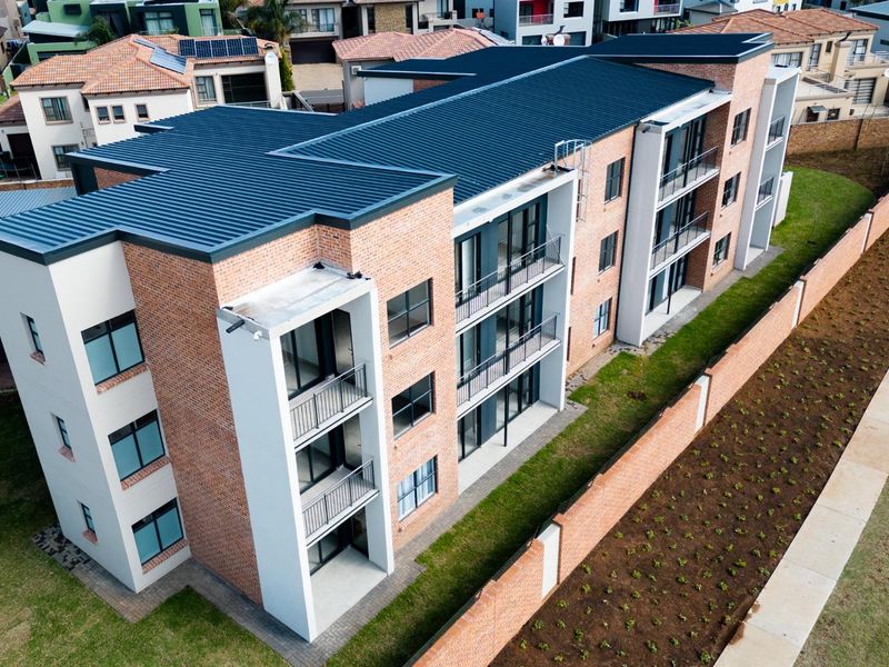 Aerial view of a modern multi-story apartment complex featuring brick and render facade, metal roofing, and private balconies.