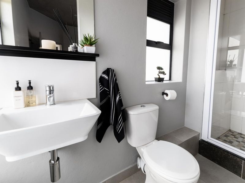 Modern bathroom featuring a wall-mounted basin, toilet, and a separate shower enclosure with tiled flooring and contemporary black window frames.