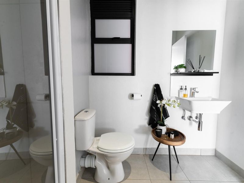 A clean, modern bathroom featuring a wall-mounted basin, a standard toilet, and a glass-enclosed shower with neutral floor tiling.