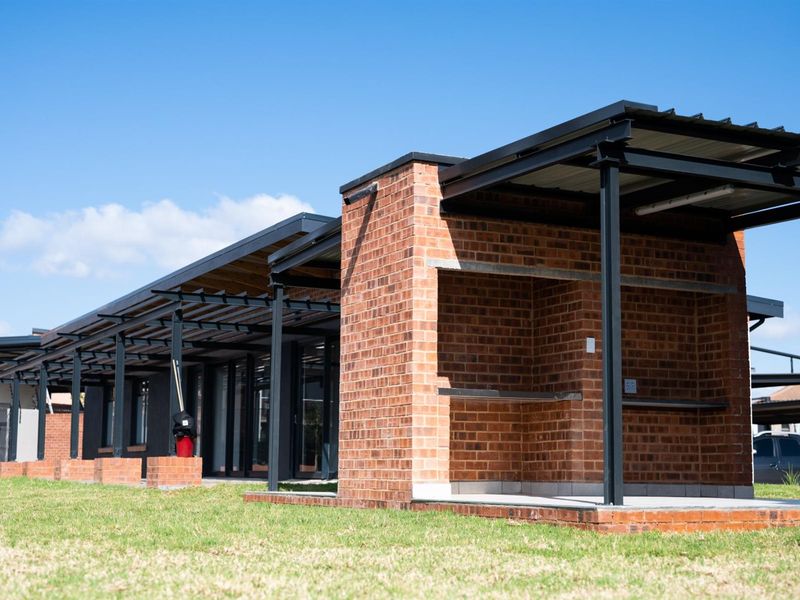 A modern exterior view featuring a covered patio area with exposed brickwork, steel structural framing, and a built-in braai facility.