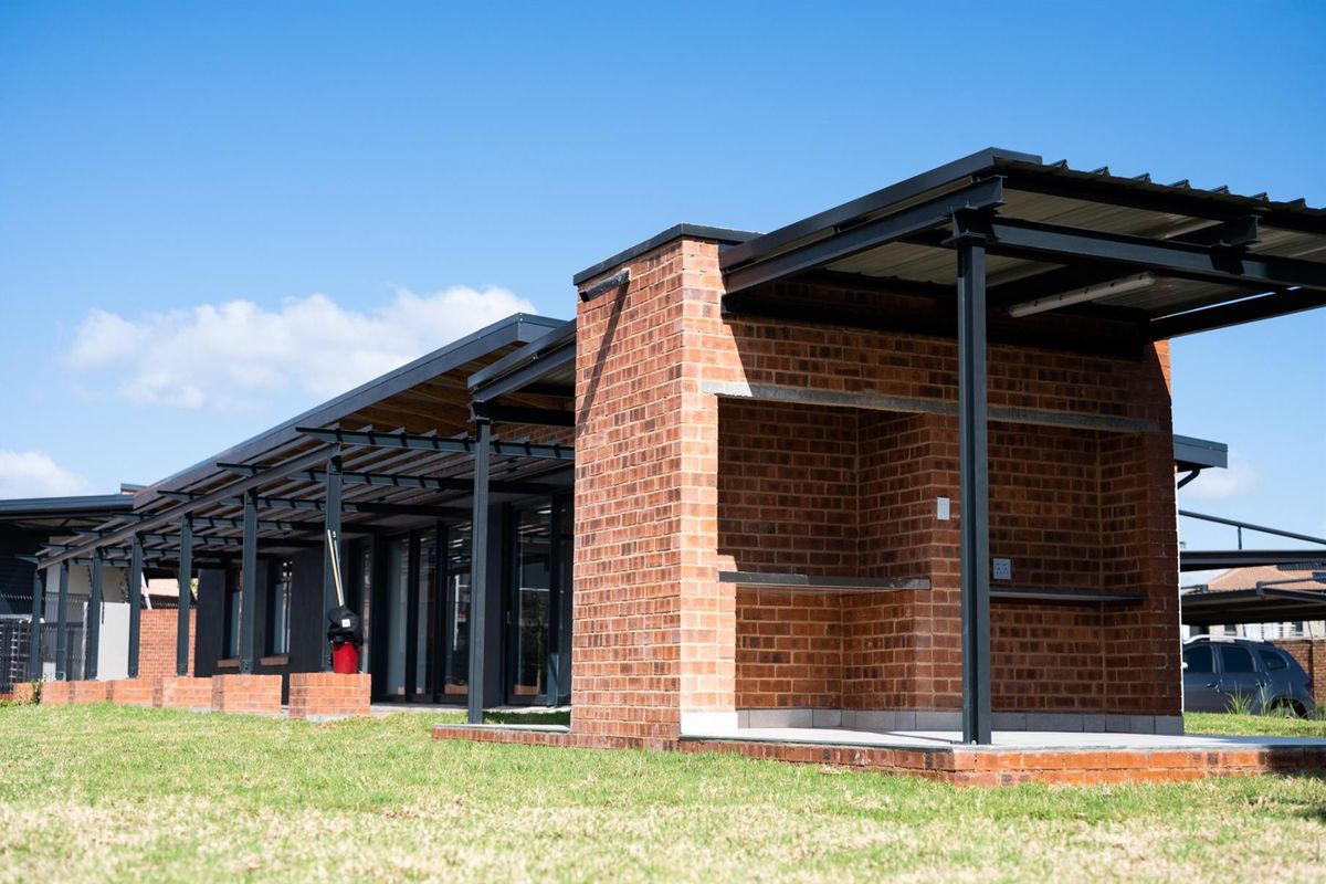 A modern exterior view featuring a covered patio area with exposed brickwork, steel structural framing, and a built-in braai facility.