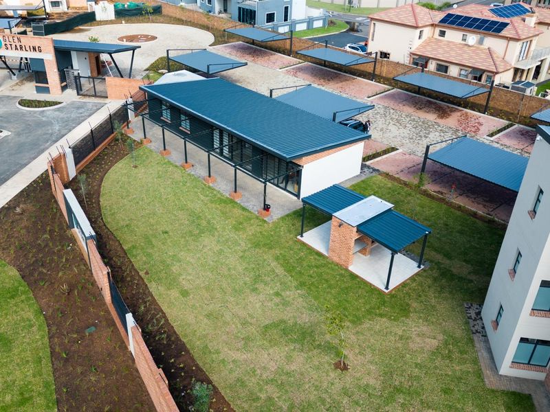 Aerial view of the apartment complex grounds, featuring a well-maintained lawn, covered parking bays, and a communal brick braai area.