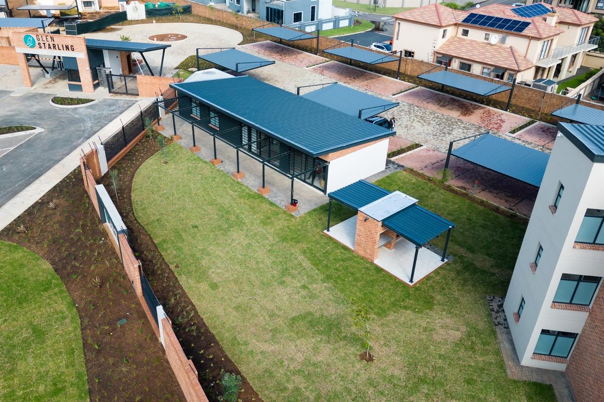Aerial view of the apartment complex grounds, featuring a well-maintained lawn, covered parking bays, and a communal brick braai area.