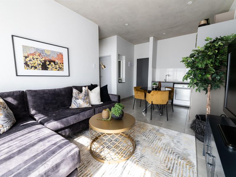 Modern open-plan living area featuring a compact kitchenette with built-in cabinetry, tiled flooring, and an exposed concrete ceiling.