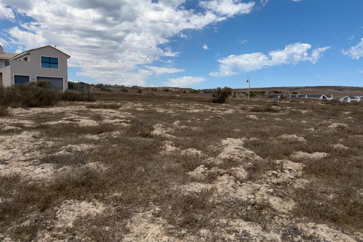 A vacant residential plot featuring natural coastal vegetation and sandy terrain, offering a blank canvas for future development in a quiet neighborhood.