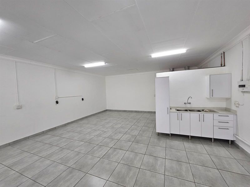 A clean, open-plan office space featuring tiled flooring, a kitchenette with built-in cabinetry, and functional overhead lighting.