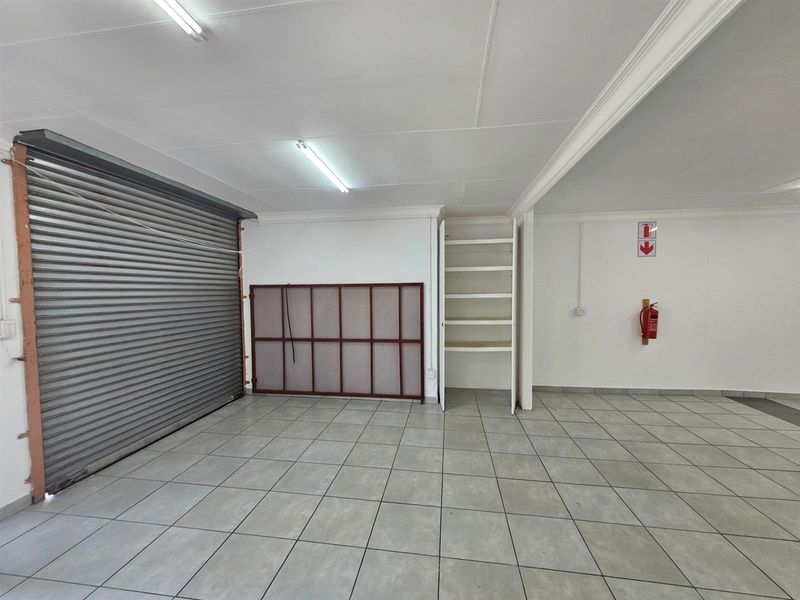 A functional office or utility space featuring tiled flooring, a roller shutter door, built-in shelving, and a wall-mounted fire extinguisher.