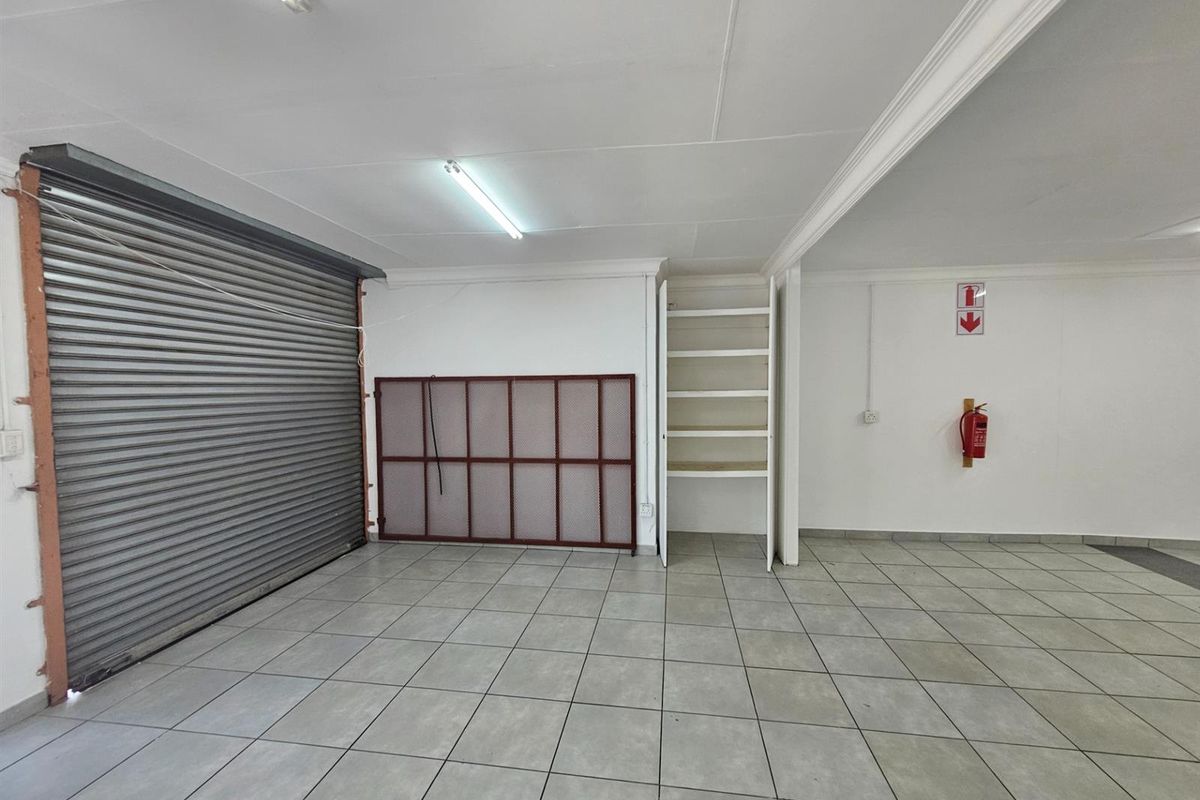A functional office or utility space featuring tiled flooring, a roller shutter door, built-in shelving, and a wall-mounted fire extinguisher.