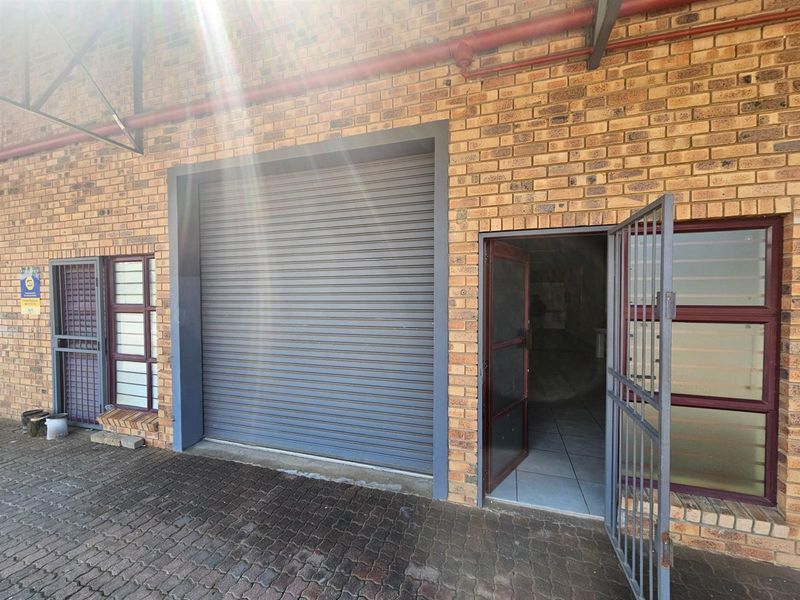 Exterior view of an office unit featuring a roller shutter door, a pedestrian entrance with security gate, and exposed brick facade.