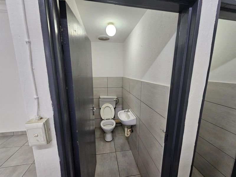 A compact office restroom featuring a standard toilet, wall-mounted basin, and neutral tiled flooring and wall accents.