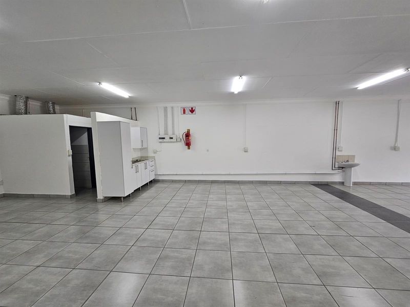 Spacious open-plan office area featuring tiled flooring, a small kitchenette unit, a wall-mounted basin, and fluorescent lighting.