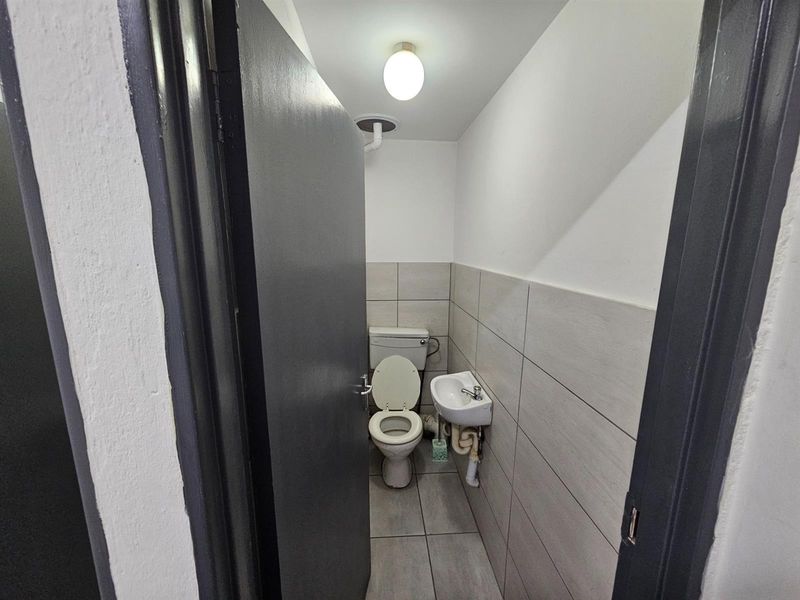 A compact office restroom featuring tiled walls and flooring, equipped with a standard toilet and a small wall-mounted basin.