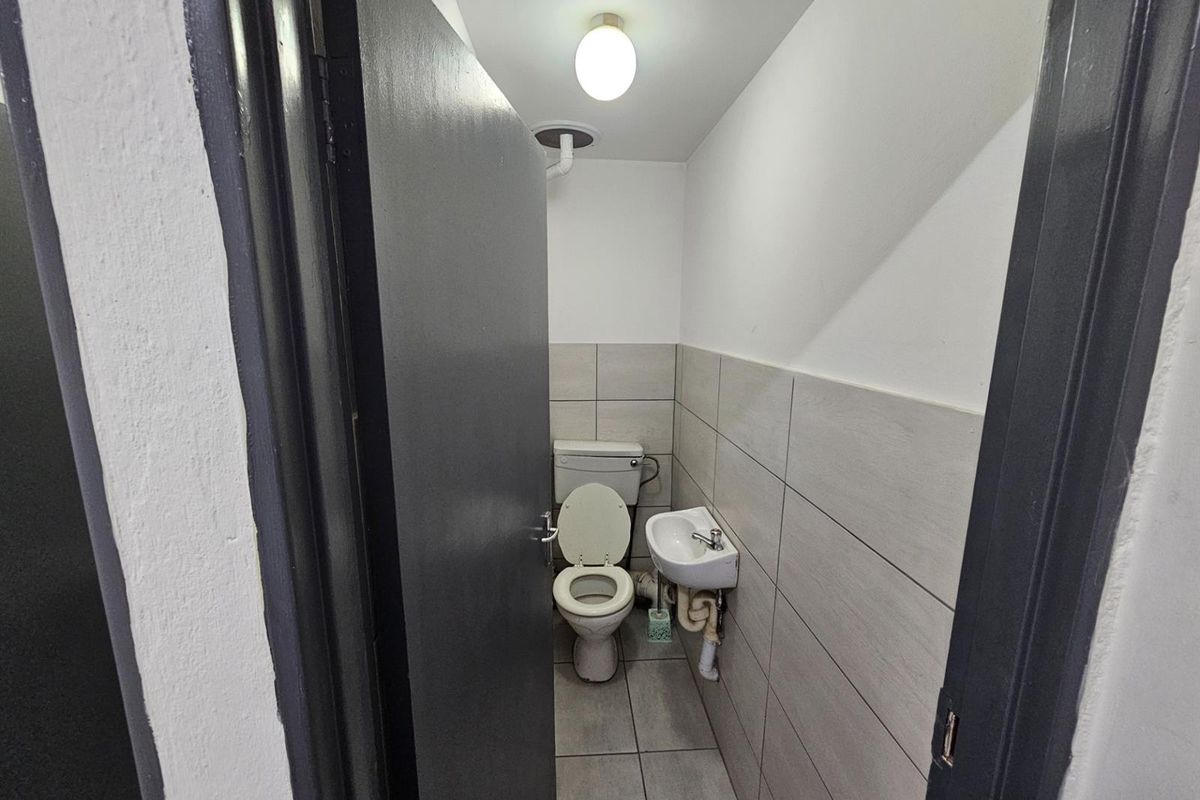 A compact office restroom featuring tiled walls and flooring, equipped with a standard toilet and a small wall-mounted basin.