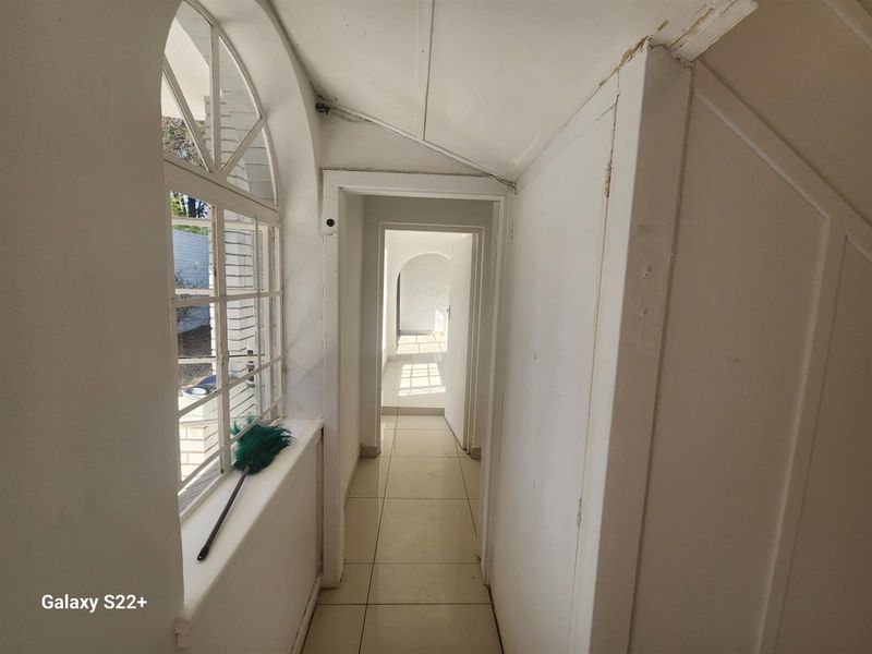 A bright hallway featuring tiled flooring, an arched window, and a series of doorways leading through the home.