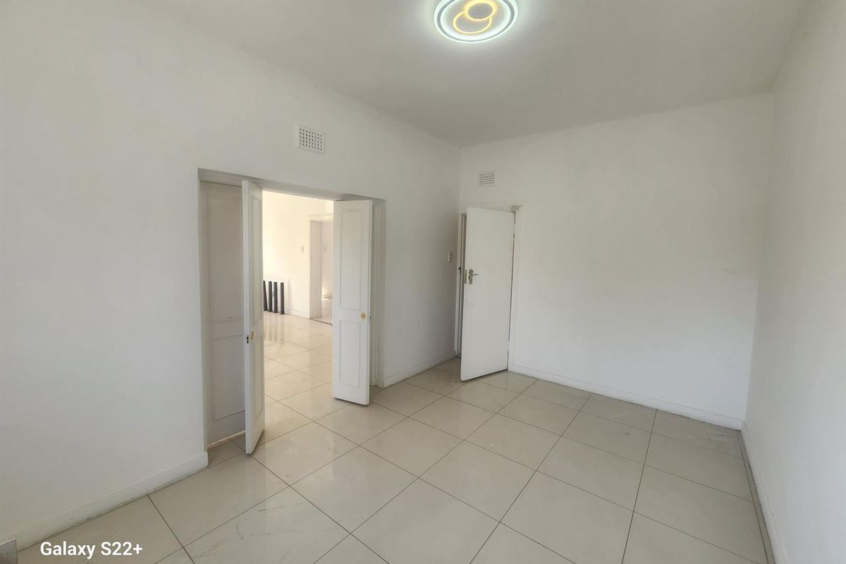 A bright, empty bedroom featuring neutral floor tiles, white walls, and multiple doorways leading to adjacent living spaces.