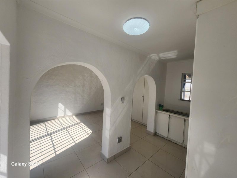 An interior view of a living area featuring arched architectural details, tiled flooring, and a small kitchenette area with built-in cabinetry.