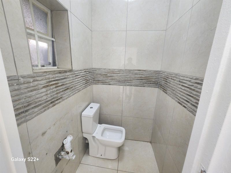 A compact bathroom featuring floor-to-ceiling tiled walls with a decorative stone-look border and a standard white toilet.