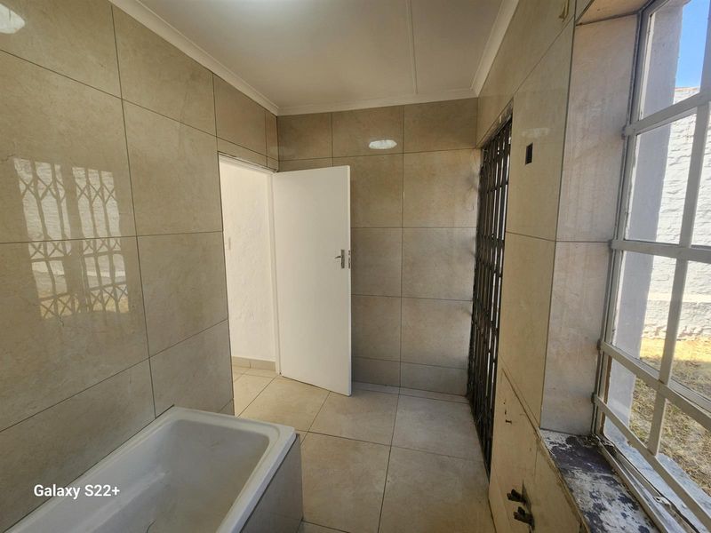 A tiled bathroom featuring a bathtub, large window with security bars, and a door leading to an adjacent room.