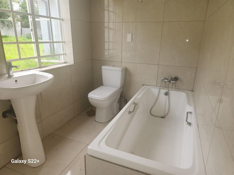 A functional bathroom featuring a pedestal basin, a standard toilet, and a built-in bathtub with wall-mounted shower fixtures and tiled finishes.