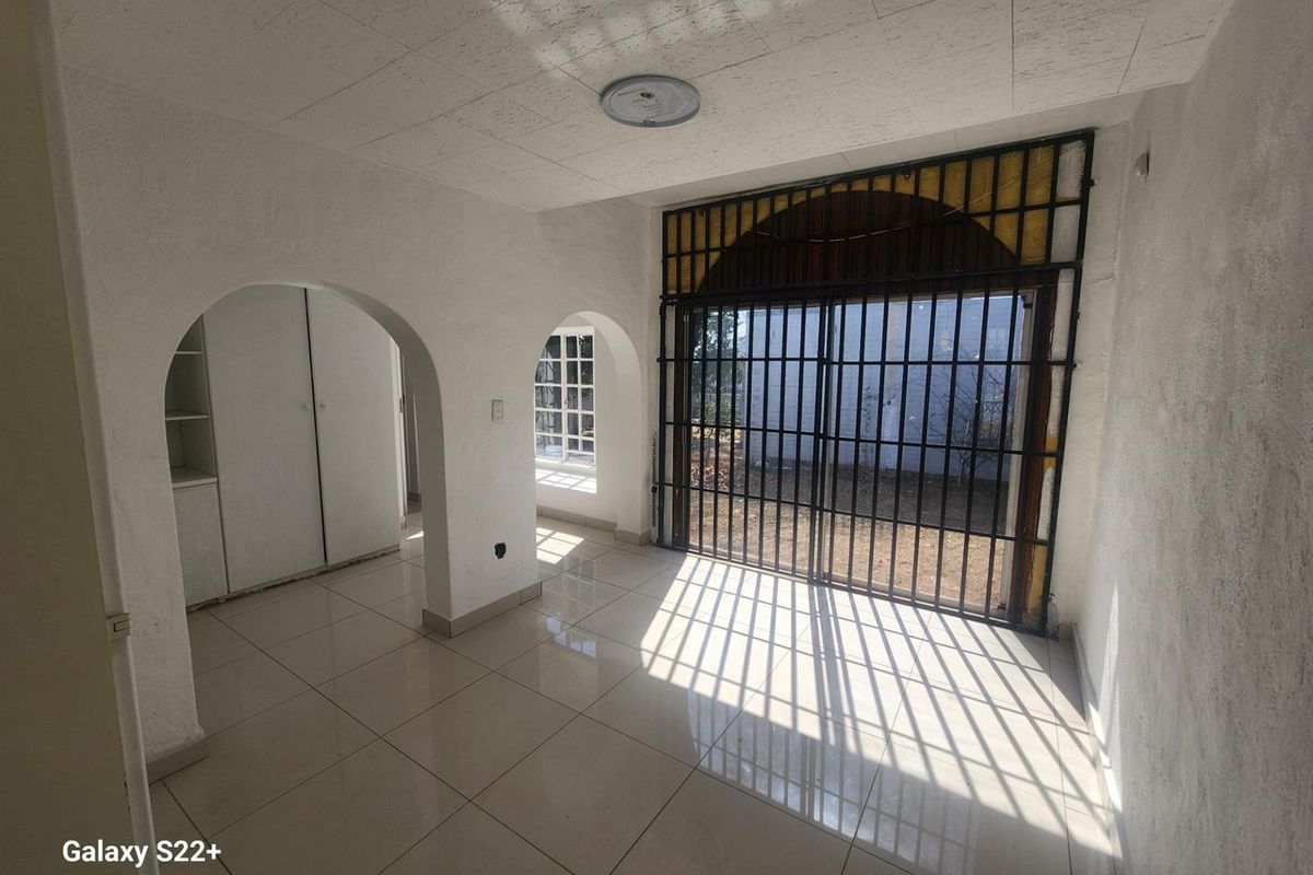 An empty living area featuring tiled flooring, arched doorways, built-in storage, and a large security-gated sliding door leading to the exterior.