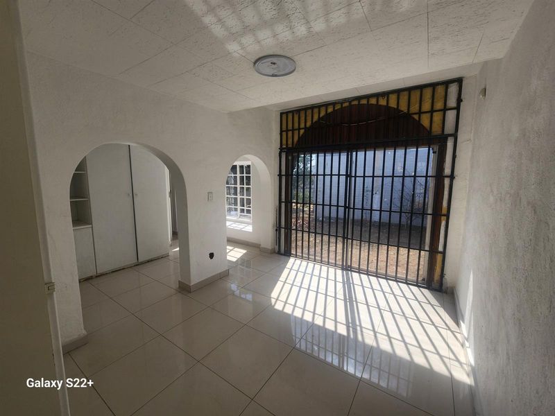 An empty living area featuring tiled flooring, arched doorways, built-in storage, and a large security-gated sliding door leading to the exterior.