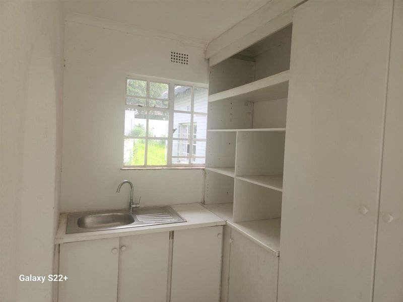 A functional scullery or utility area featuring built-in cabinetry, open shelving, and a stainless steel sink with a window view.