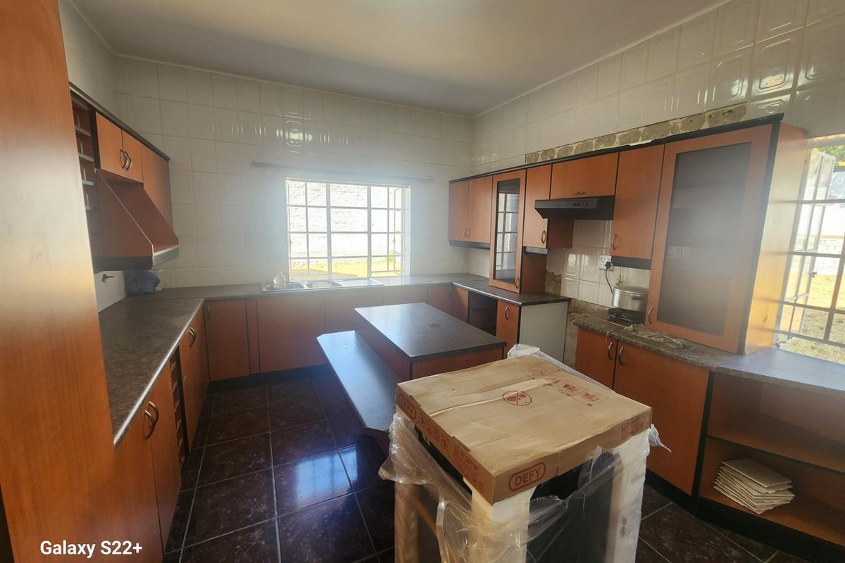 A functional kitchen featuring wooden cabinetry, dark countertops, tiled flooring, and a central island, offering a practical layout for meal preparation.