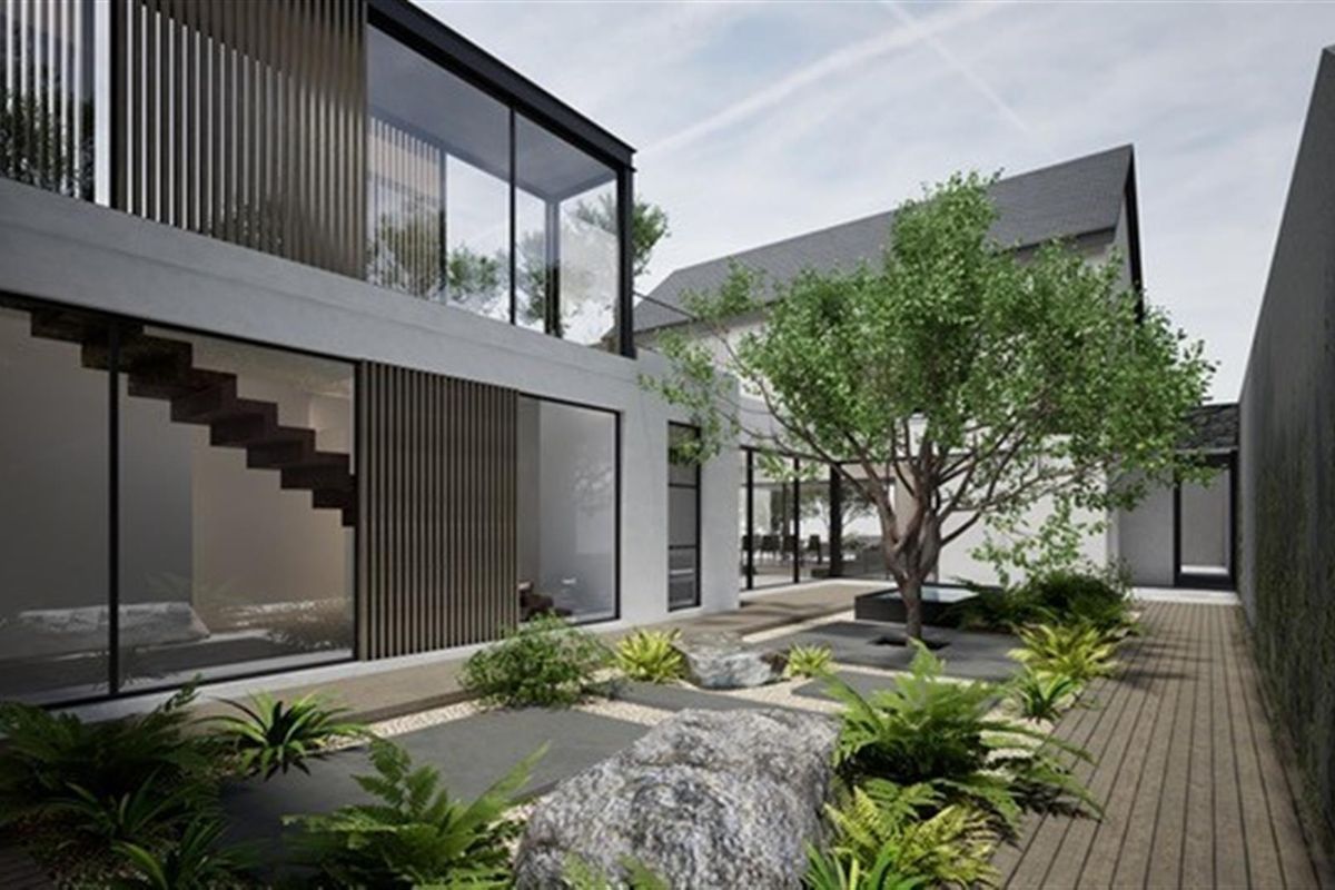A modern architectural exterior view featuring a landscaped courtyard with stone elements, timber decking, and large glass windows connecting indoor and outdoor spaces.