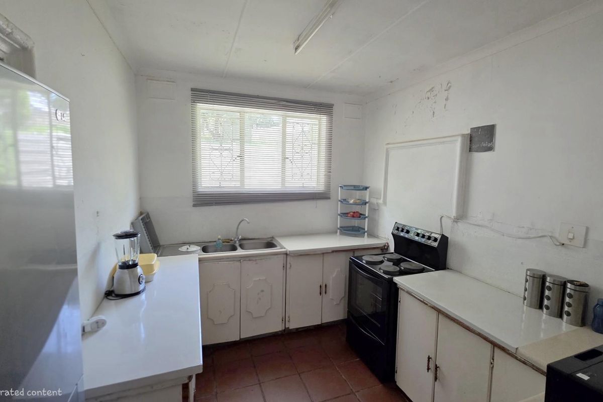 A dated kitchen featuring basic cabinetry, a double sink, and a freestanding stove, requiring cosmetic updates and wall repairs.